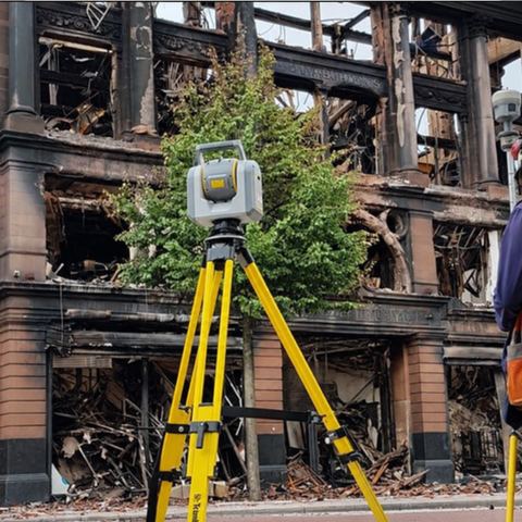 Estación total frente a un edificio con daños de incendio.