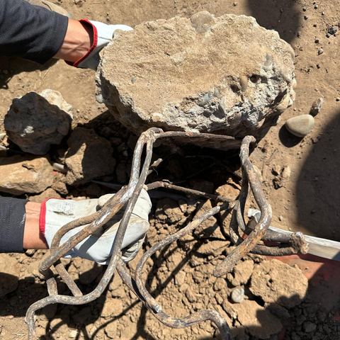 Fragmento de hormigón con enfierradura expuesta en manos enguantadas.